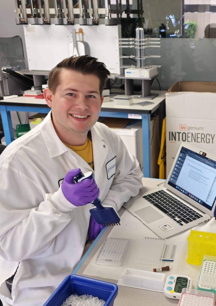 Biotech lab technician using multichannel pipette at bench with laptop, PCR plates, ice and research equipment