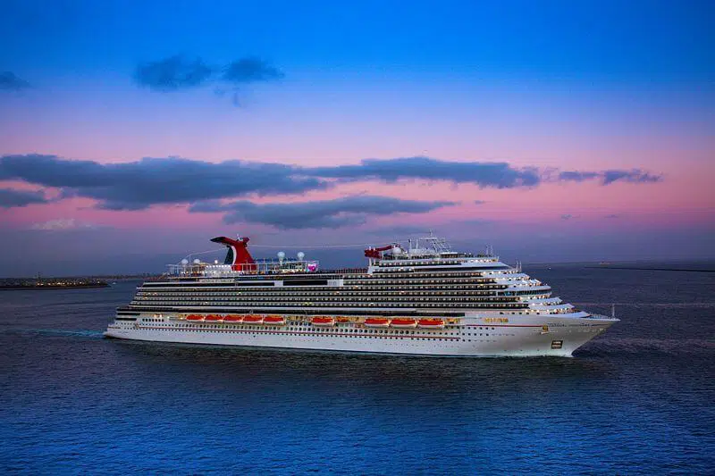 Cruise ship sailing at sunset with colorful sky and ocean in the background.