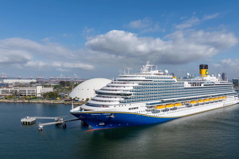 Cruise ship docked at a sunny port with white domed terminal building in the background.